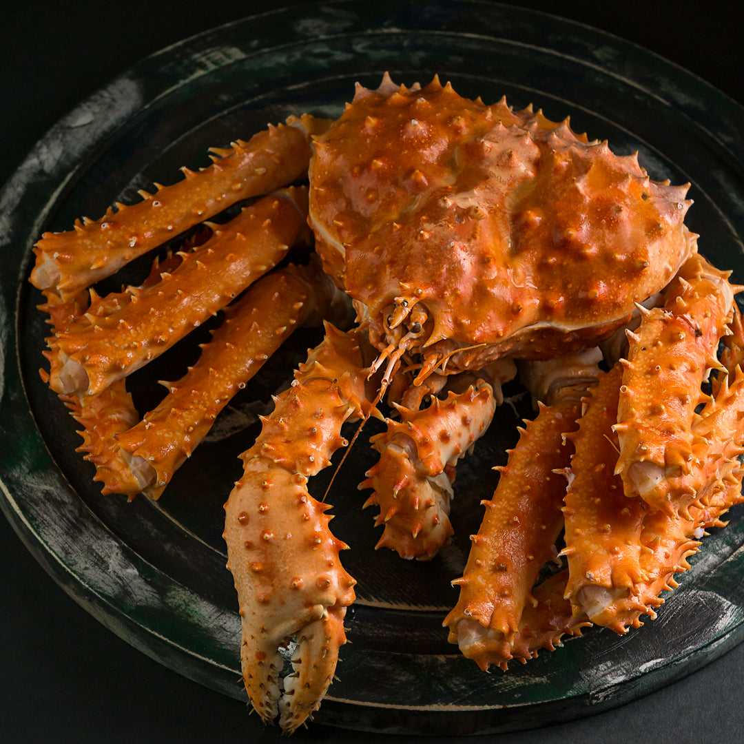 Whole cooked king crab served on a black plate, showcasing its bright red shell and impressive size
