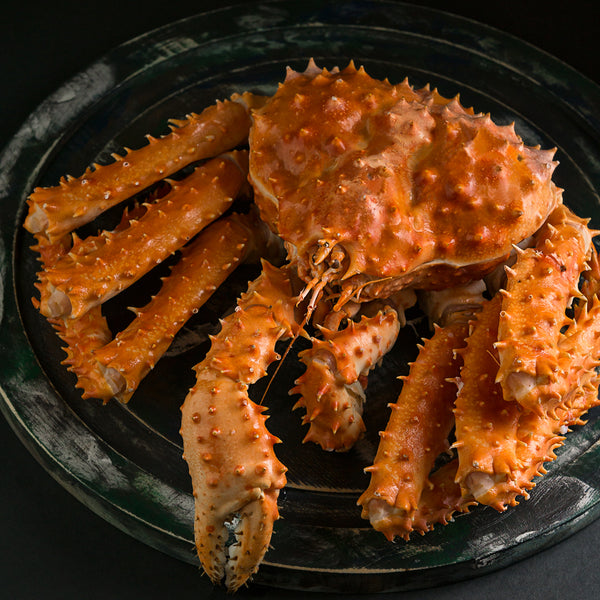 Whole cooked king crab served on a black plate, showcasing its bright red shell and impressive size