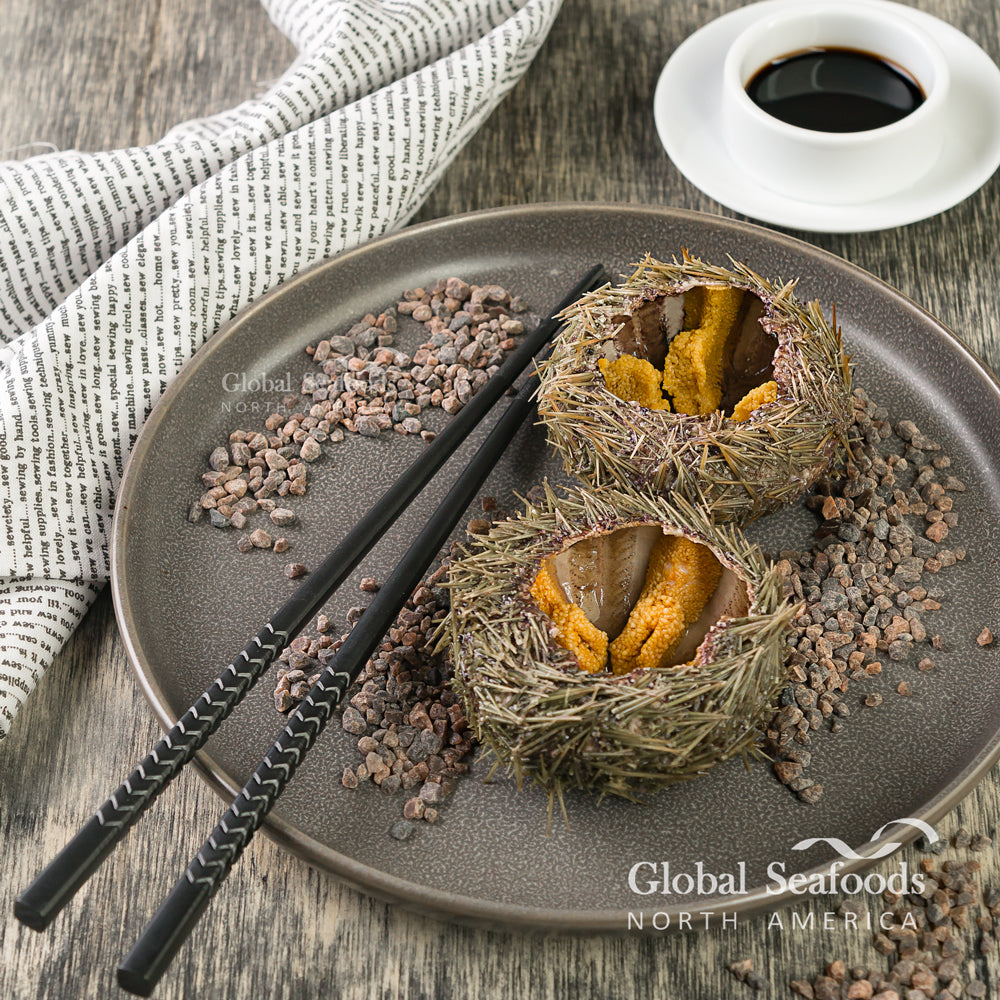 Freshly opened sea urchins with bright uni displayed on a sleek black plate, accompanied by chopsticks for a luxurious sashimi-style presentation