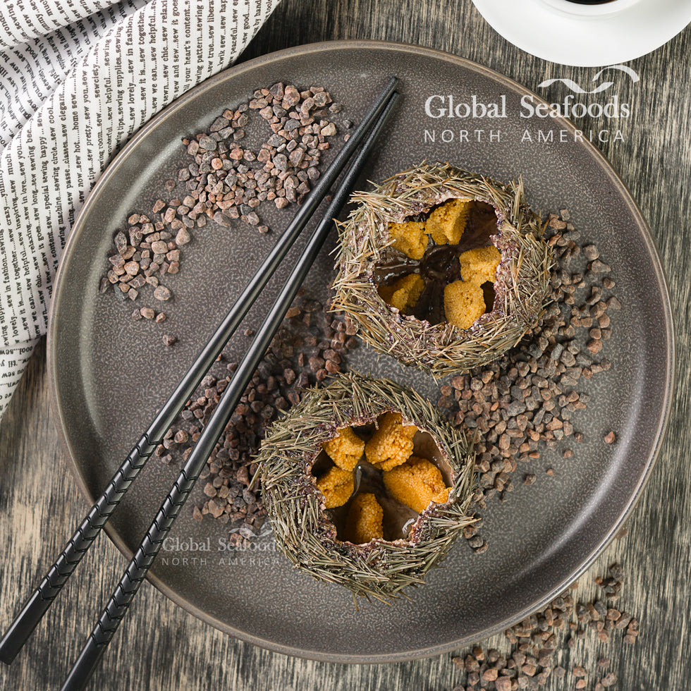 Two fresh sea urchins opened on a black plate, revealing golden uni (roe) inside, served with chopsticks for a refined seafood presentation