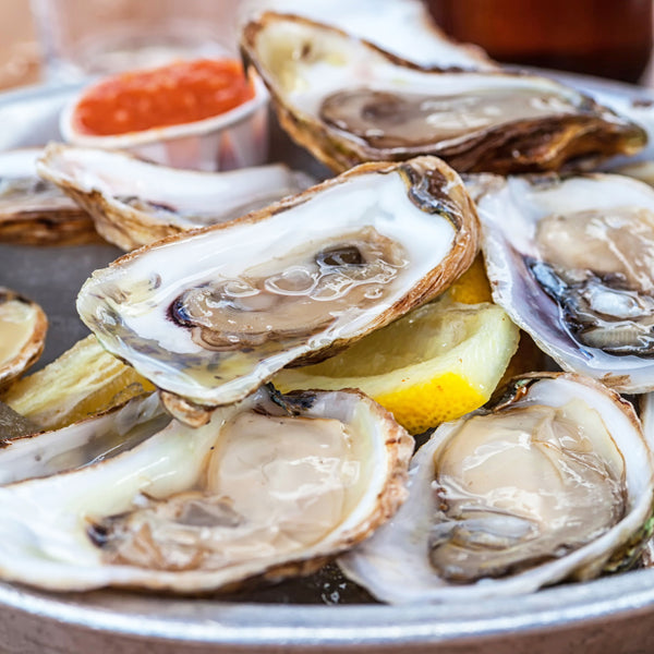 Opened oysters on a plate with dipping sauce and lemon