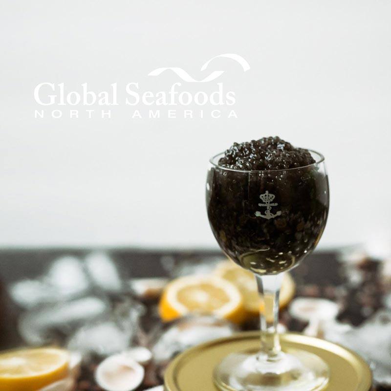 Sevruga caviar in a stemmed glass on a gold tin, with lemon slices and seashells in the background