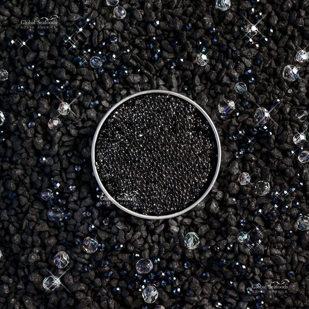 Overhead view of an open tin of Hackleback caviar on black pebbles with decorative beads