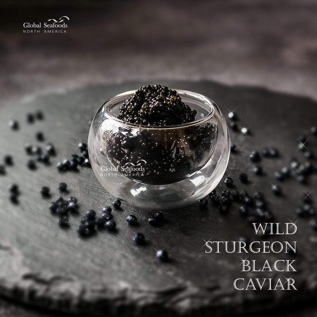 Hackleback caviar in a clear double-walled glass bowl on slate, surrounded by black decorative beads