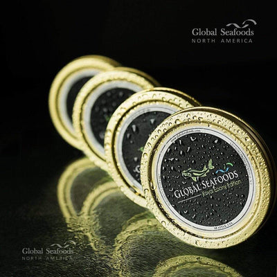 Four tins of black caviar standing side by side, with water droplets on the lids and a dark, softly lit background, creating a luxurious and chilled seafood presentation