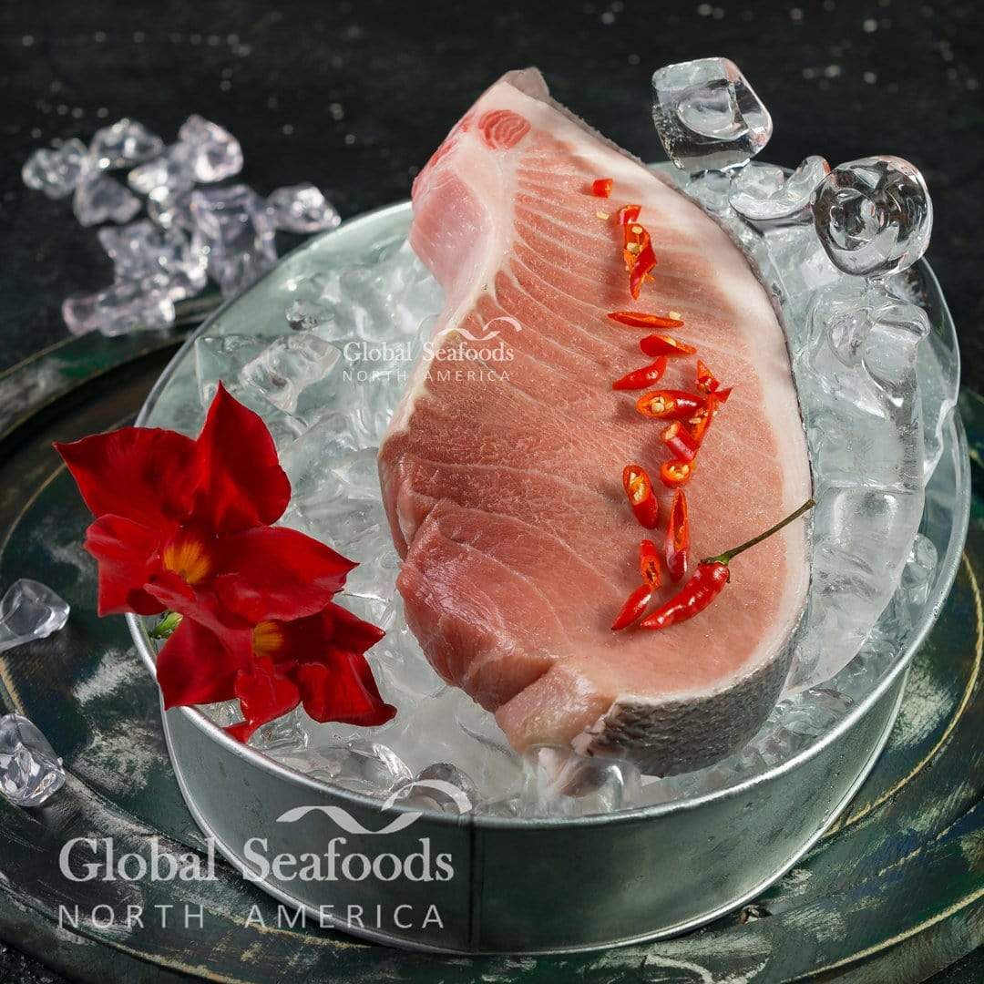 Raw skin-on bluefin tuna belly steak on ice in a metal tray, topped with sliced red chilies.