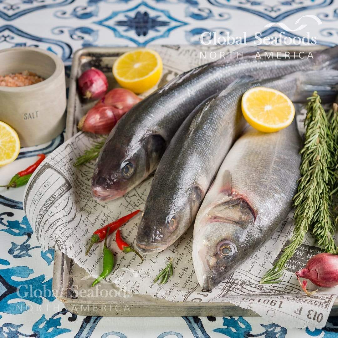 Three whole branzino on paper in a tray with lemon and shallots.