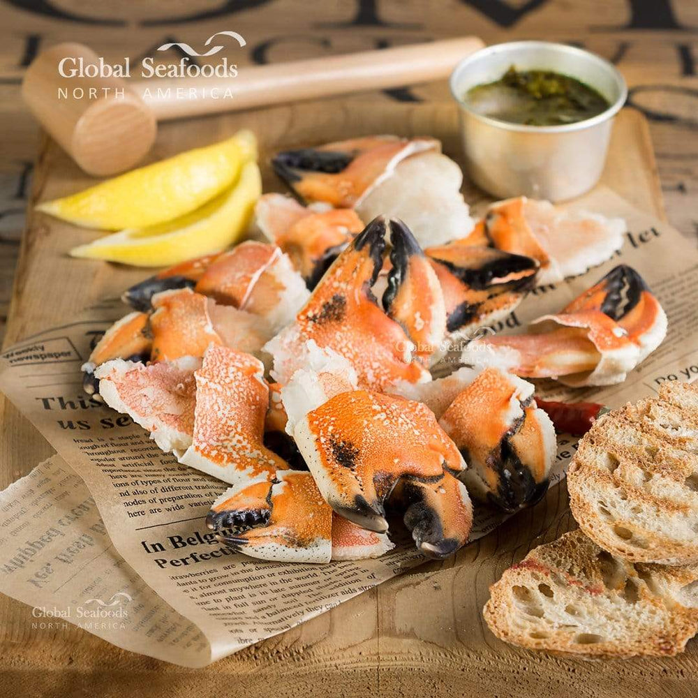 Jonah crab claws placed on newspaper atop a wooden desk, with a crab hammer in the background and two slices of toast on the side, styled for a rustic and casual seafood presentation