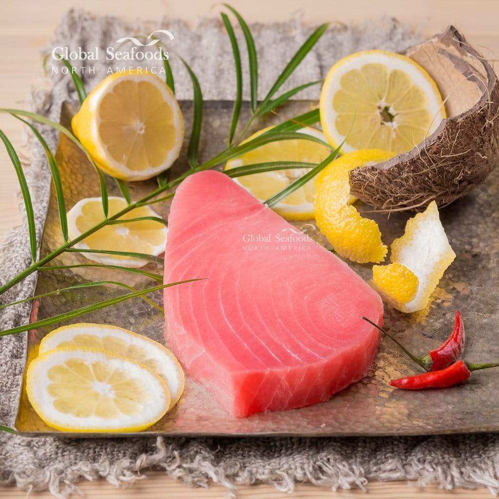 Raw yellowfin tuna steak on a metal tray with lemon slices and coconut