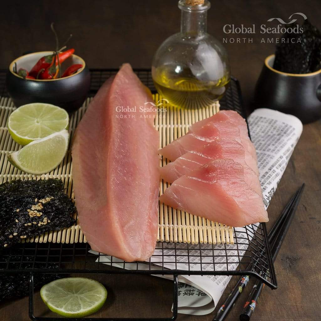 Albacore tuna loin and slices on a bamboo mat with lime wedges and nori