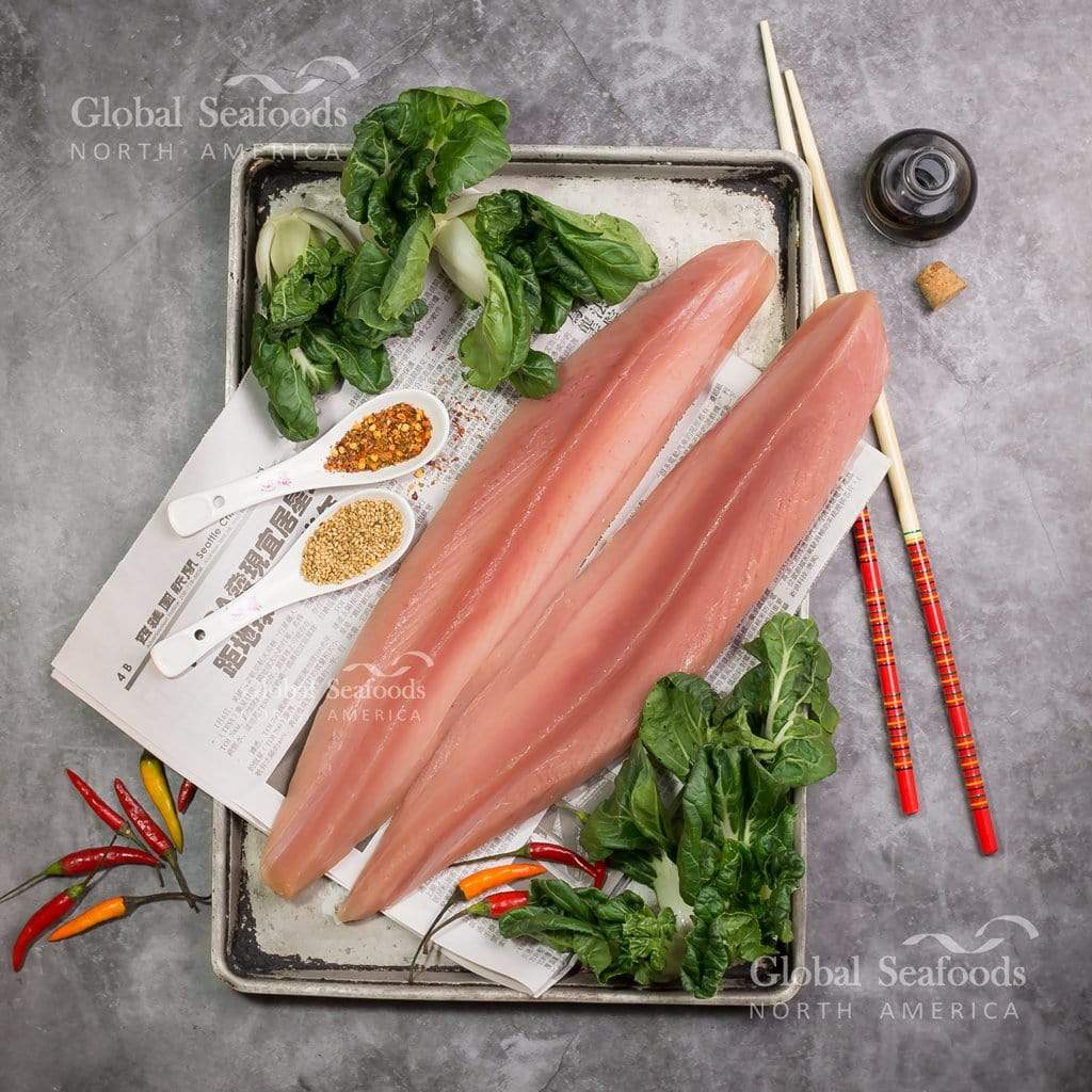 Two raw albacore tuna loins on a metal tray with leafy greens, seasonings and chopsticks