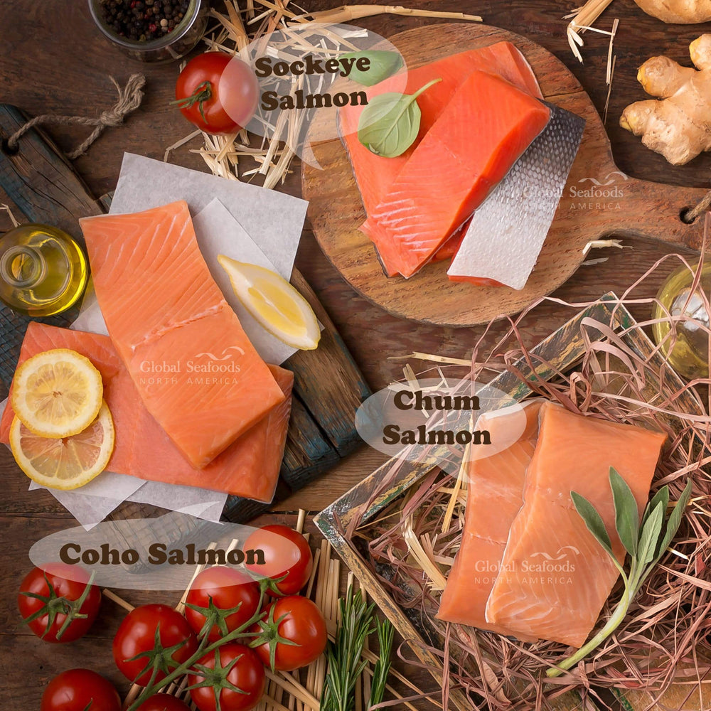 Three types of salmon displayed for comparison: two Coho salmon portions skin-side down on a wooden board with a glass bottle of oil and lemon; two Sockeye salmon portions skin-down and one skin-up in the center on a round wooden board; and two Chum salmon fillets skin-side down placed on dried seaweed in a rectangular wooden tray. A vibrant seafood arrangement showcasing texture, color, and variety