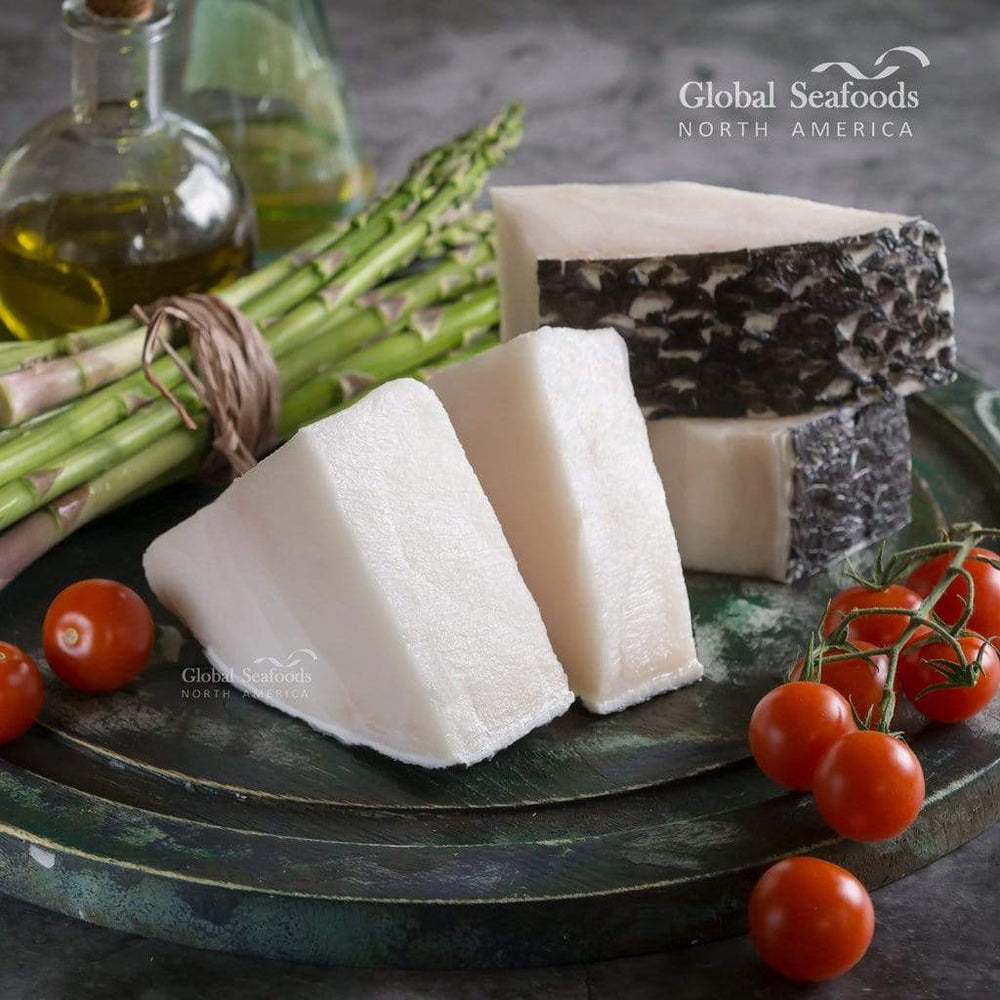 Chilean sea bass portions with skin on, served on a dark round flat plate with asparagus and cherry tomatoes for an elegant and colorful seafood dish