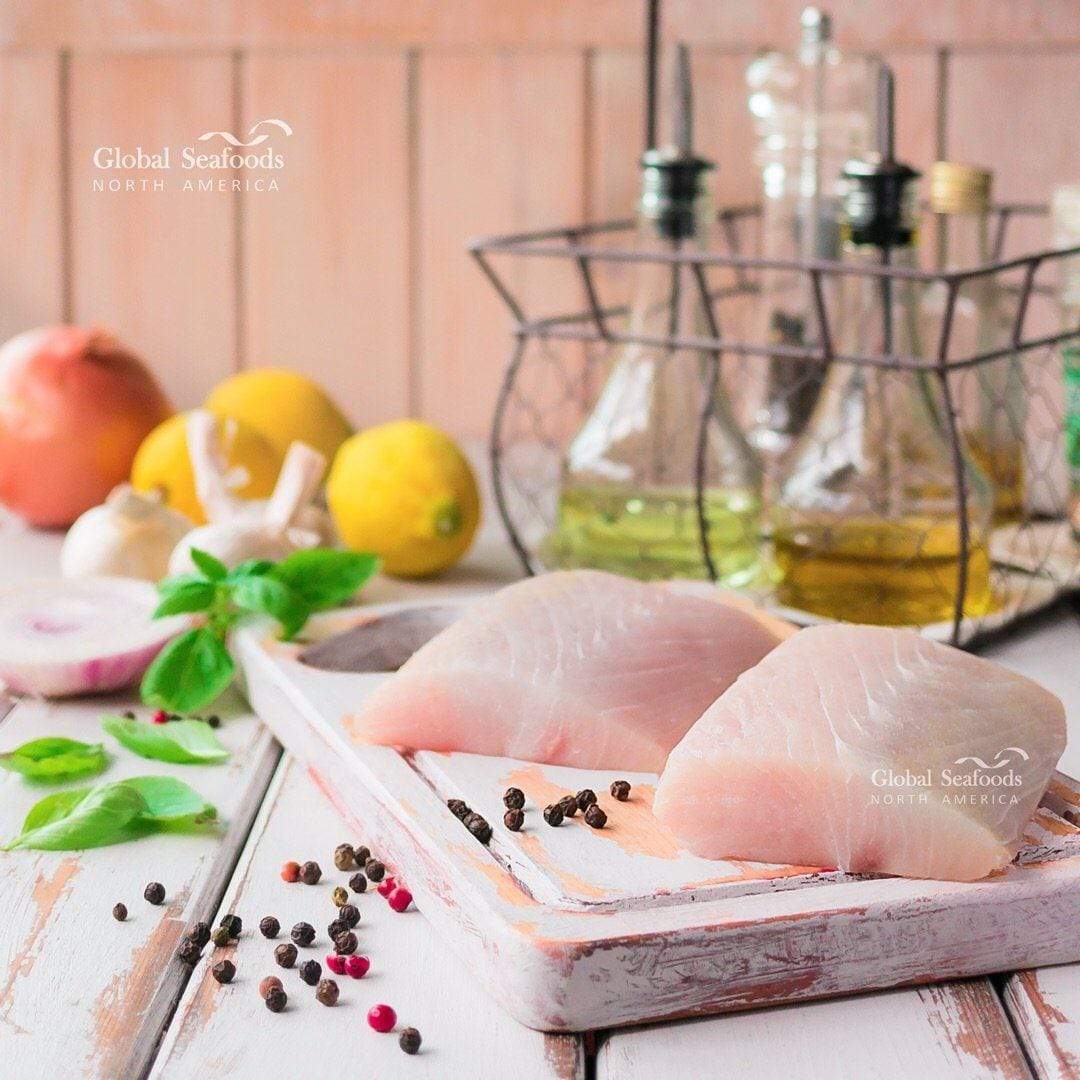 Raw mahi mahi portions on a wooden board with lemons and bottles behind
