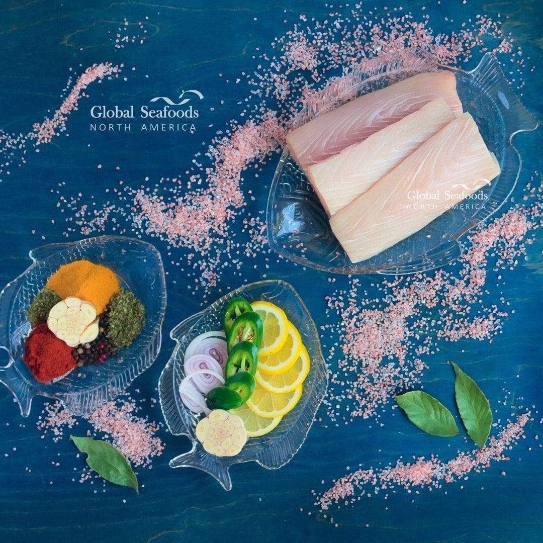 Raw mahi mahi portions on a glass plate with salt, citrus and seasonings on a blue surface