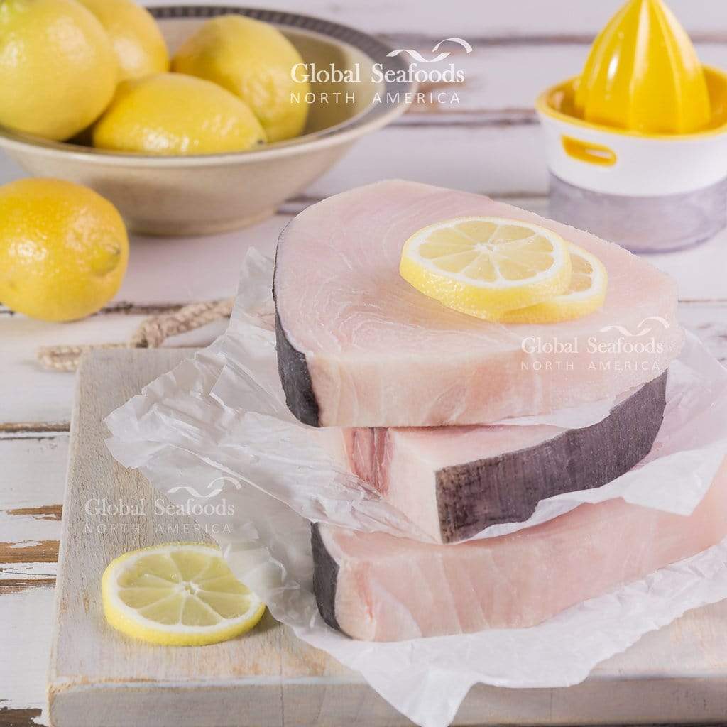 Three raw swordfish steaks stacked with parchment and lemon slices