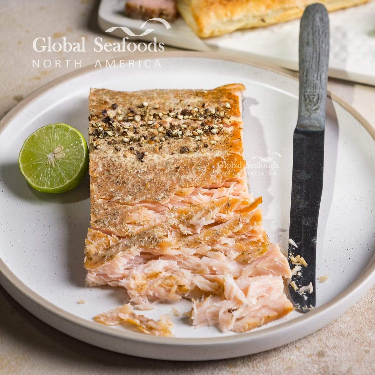 Hot-smoked king salmon on a white plate, served with a fork, knife, and half a lime, highlighting its rich texture and premium presentation