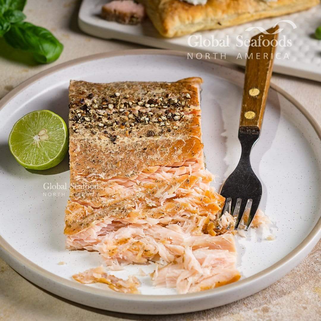 Hot-smoked king salmon served on a white plate with a fork and half a lime, showcasing its rich color and ready-to-eat gourmet quality