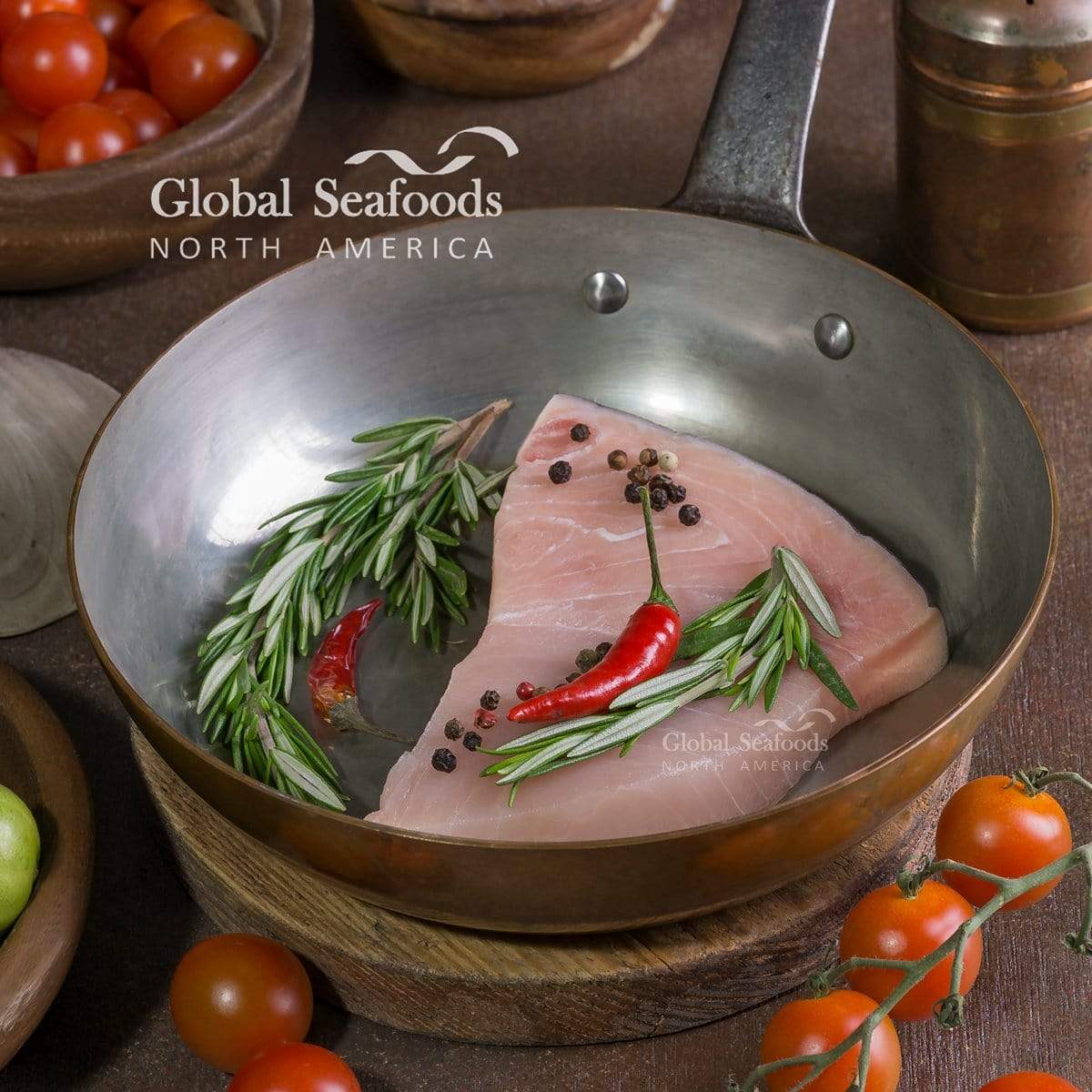 Raw swordfish steak in a frying pan with rosemary and red chilies