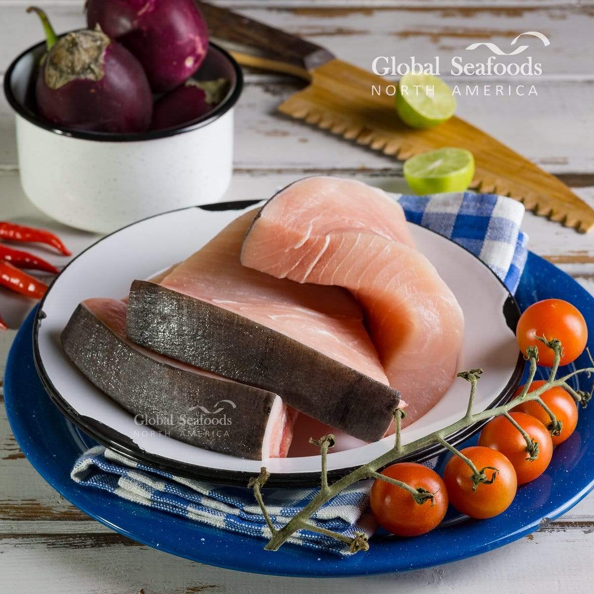 Raw swordfish steaks on a white plate with tomatoes and eggplant nearby