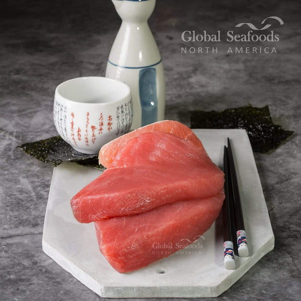 Two raw yellowfin tuna steaks stacked on a white board beside chopsticks and nori sheets.