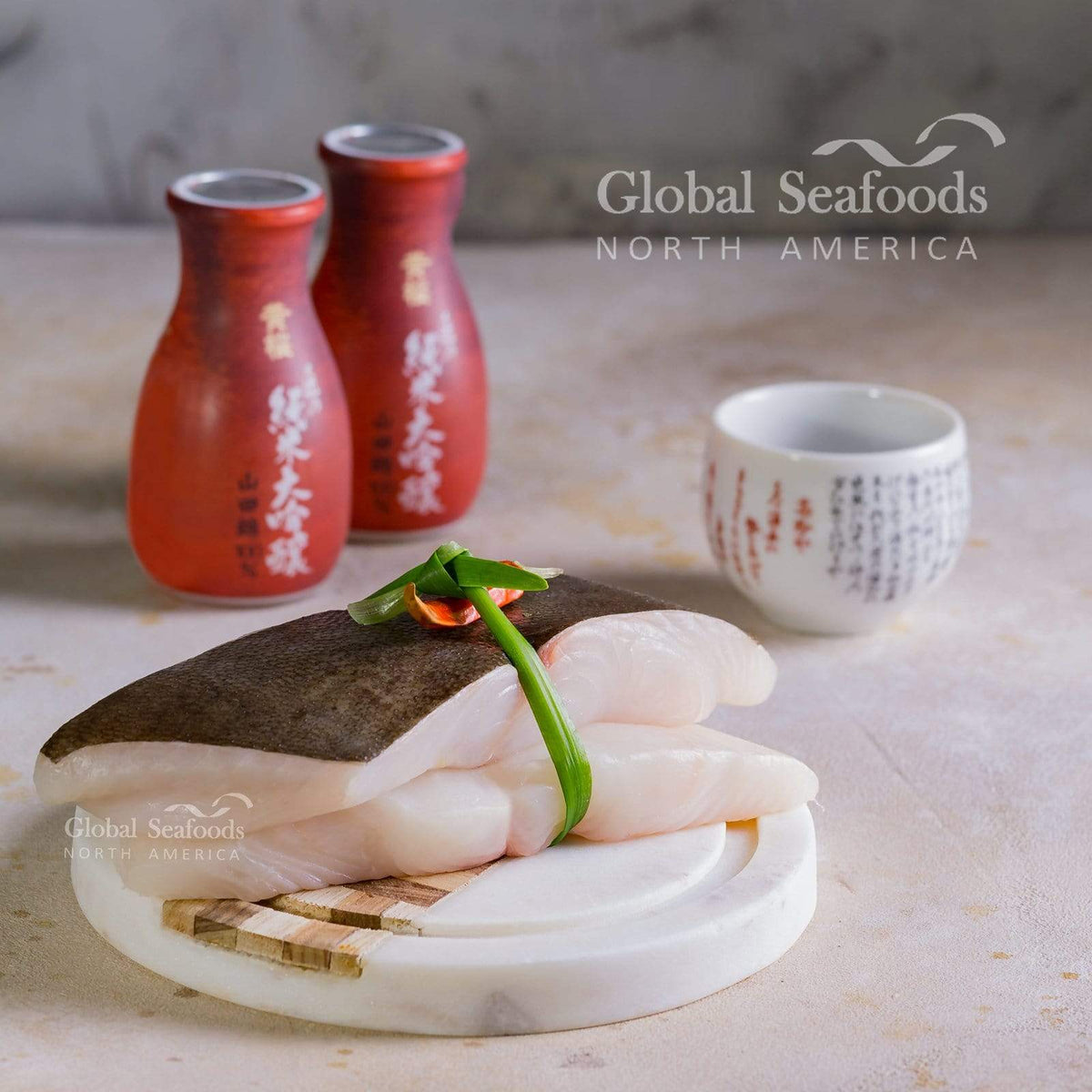 Skin-on halibut fillet portions tied with a green stem beside red bottles and a white cup.