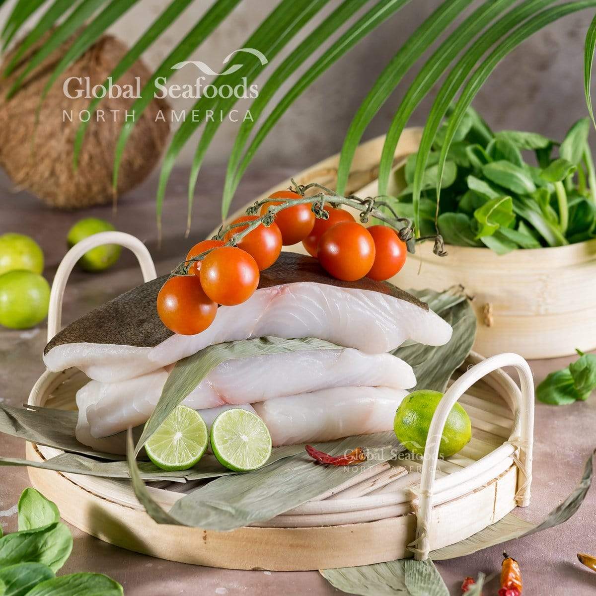 Skin-on halibut fillets stacked in a tray with lime slices and cherry tomatoes.