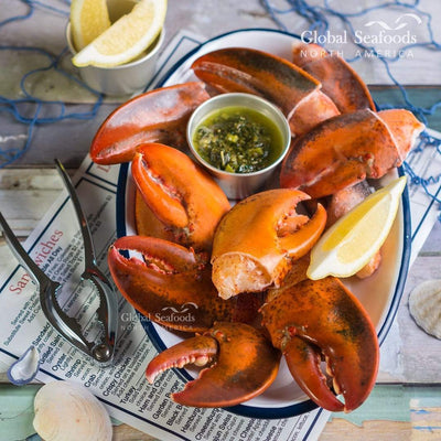 Pre-cut lobster claws arranged on a plate with dipping sauce and a slice of lemon, ready to serve as a gourmet seafood appetizer