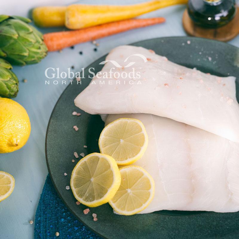 Overhead view of raw halibut fillets on a gray plate with lemon slices.