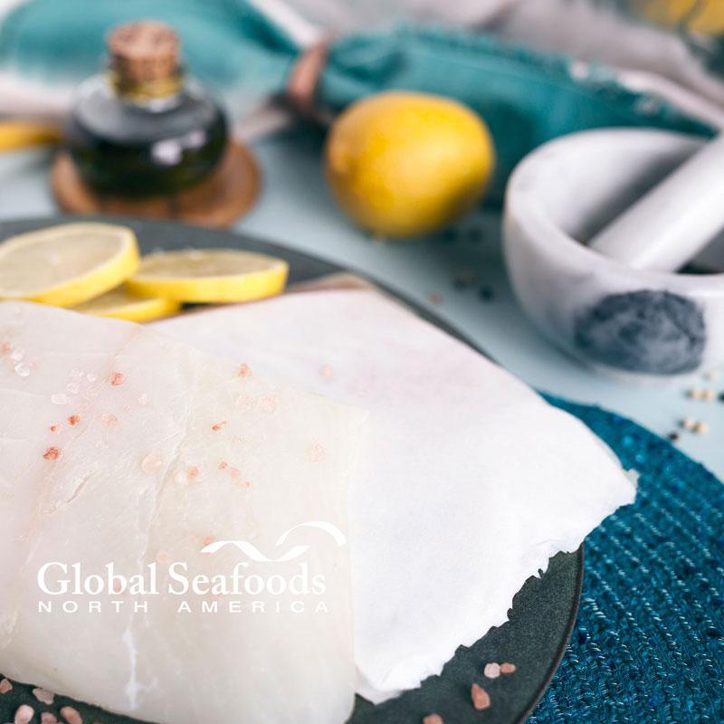 Close-up of raw halibut fillets on a plate with lemon and a mortar in the background.