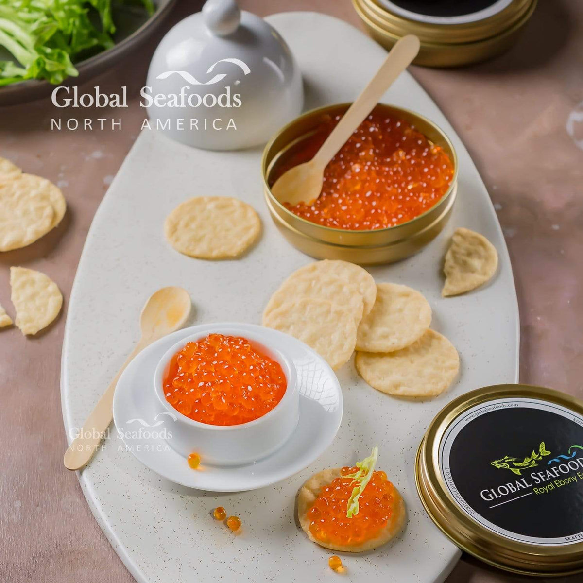 Trout roe in an open tin and white bowl on a serving platter, with crackers, wooden spoons and a caviar-topped cracker
