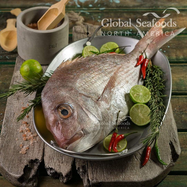 Whole snapper on a metal plate with lime slices, herbs and chilies.