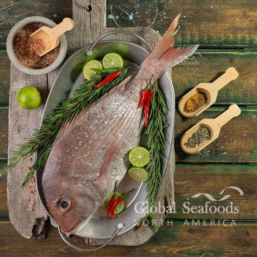 Whole snapper in an oval metal dish with lime, herbs and chilies.