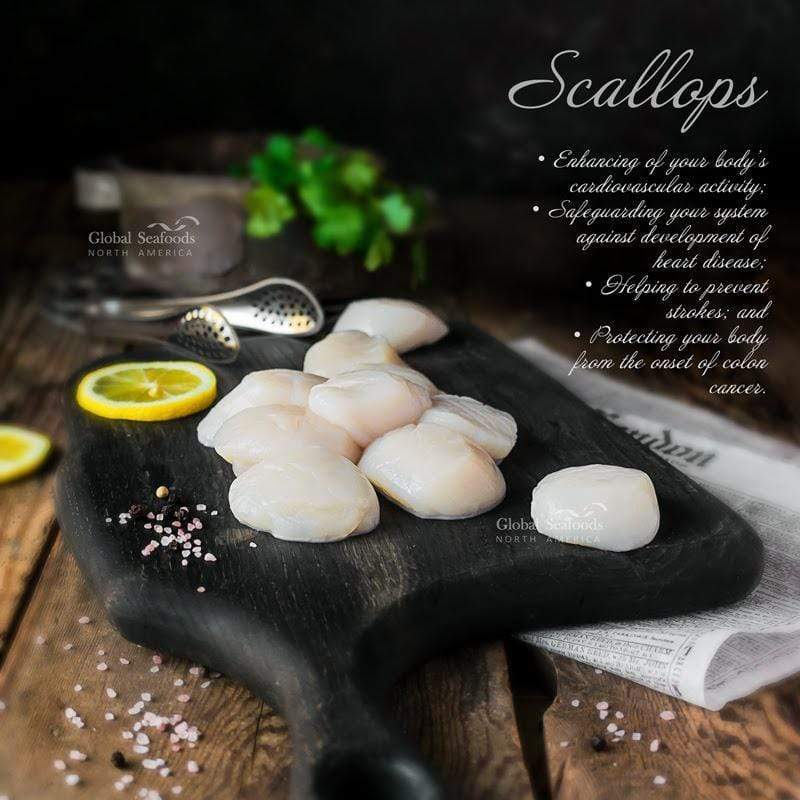 Fresh wild-caught jumbo sea scallops arranged on a black cutting board, placed on a brown table, showcasing their plump texture and premium quality for a gourmet seafood preparation