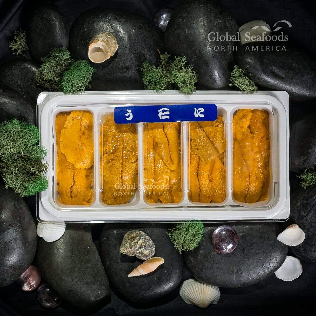 Uni (sea urchin roe) arranged in a white five-section plastic tray, placed on black rocks for a striking contrast and premium seafood presentation
