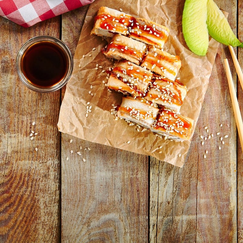 Sliced smoked sablefish with sauce and sesame seeds on a wooden board.