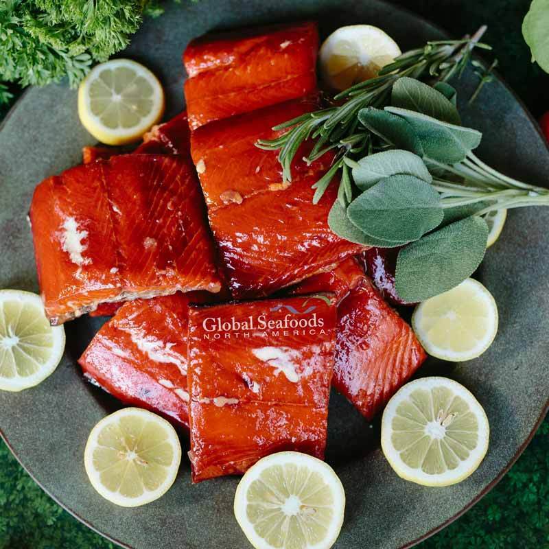 Top-down view of hot-smoked sockeye salmon portions on a green plate, garnished with lemon slices, highlighting their vibrant color and ready-to-serve quality