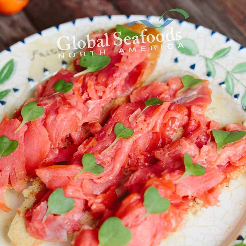 Sockeye salmon lox served on toasted bread slices, arranged on a white plate for a vibrant and elegant seafood appetizer presentation