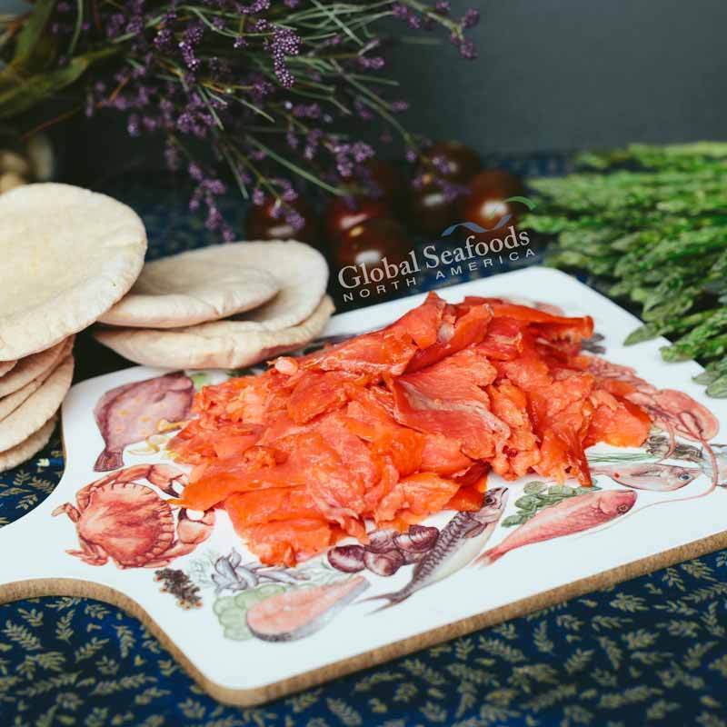 Sockeye salmon lox placed on a decorative cutting board illustrated with crab and fish drawings, served alongside flatbread for a visually engaging and gourmet seafood presentation