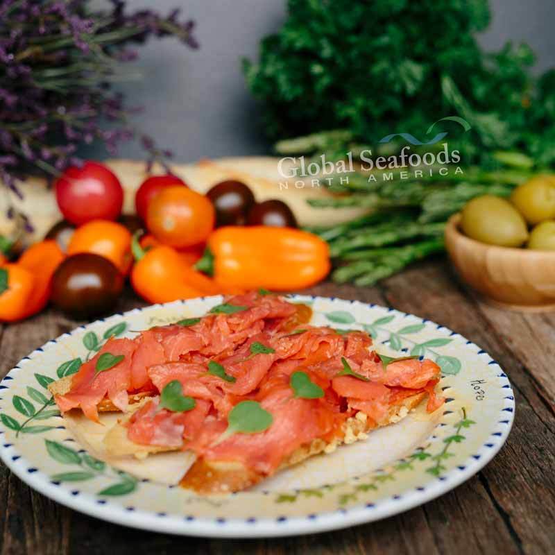 Side view of Sockeye salmon lox on toasted bread slices, served on a white plate with cherry tomatoes and a small piece of parchment paper in the background, styled for a fresh and appetizing seafood dish