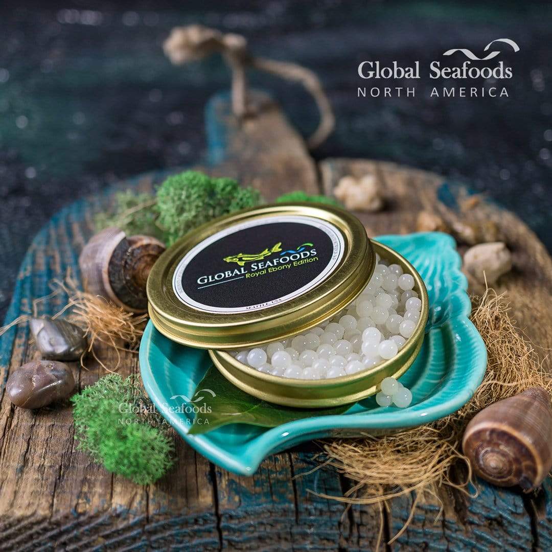 White snail caviar in a gold tin with its lid partly open on a turquoise leaf-shaped plate, beside snail shells