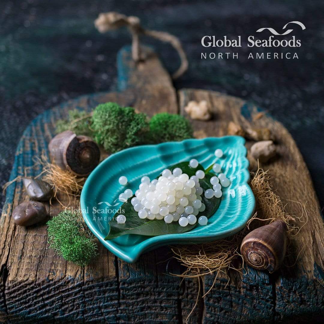 White snail caviar pearls on a green leaf in a turquoise plate, with snail shells on a rustic wooden board