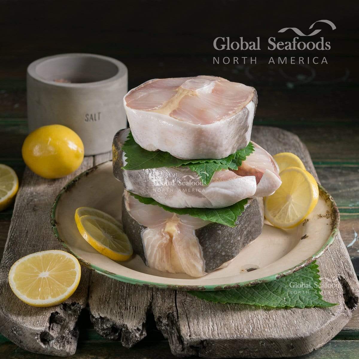 Three raw sturgeon steaks stacked with green leaves on a plate with lemon slices.