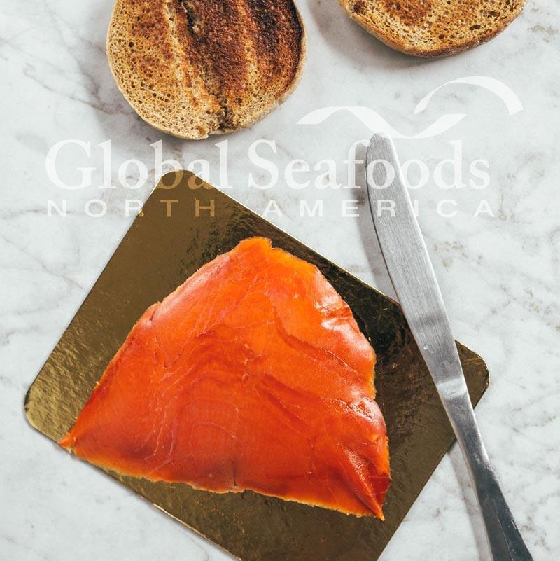 Coho salmon lox neatly arranged on a golden tray, served with two toasted bagels on the side for a classic and elegant seafood brunch presentation