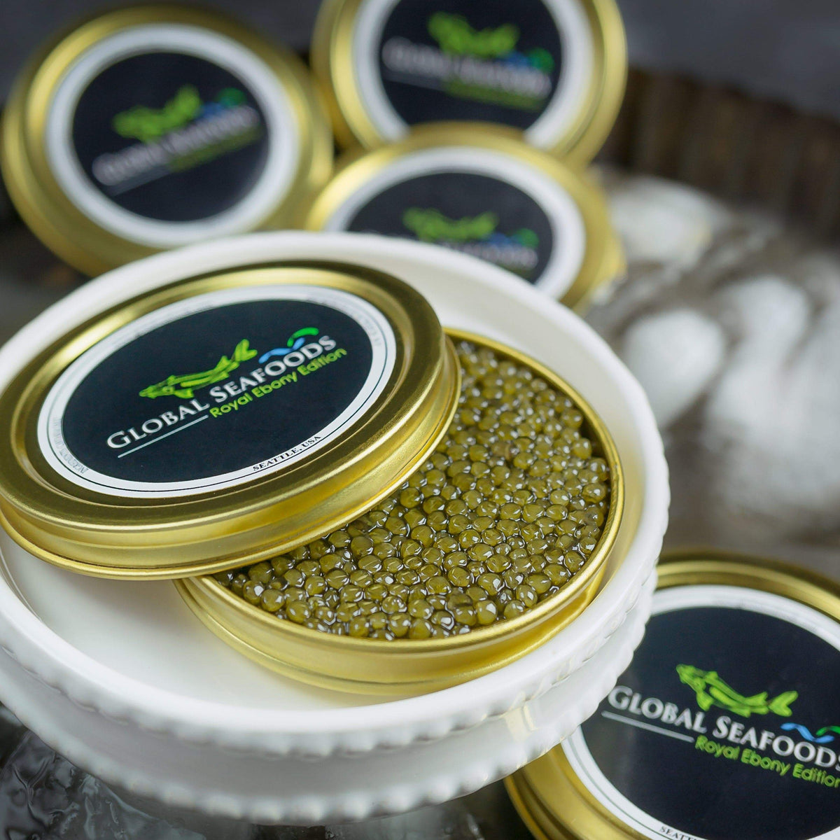 Ossetra caviar in a gold-colored tin with its lid partly covering the roe on a white plate