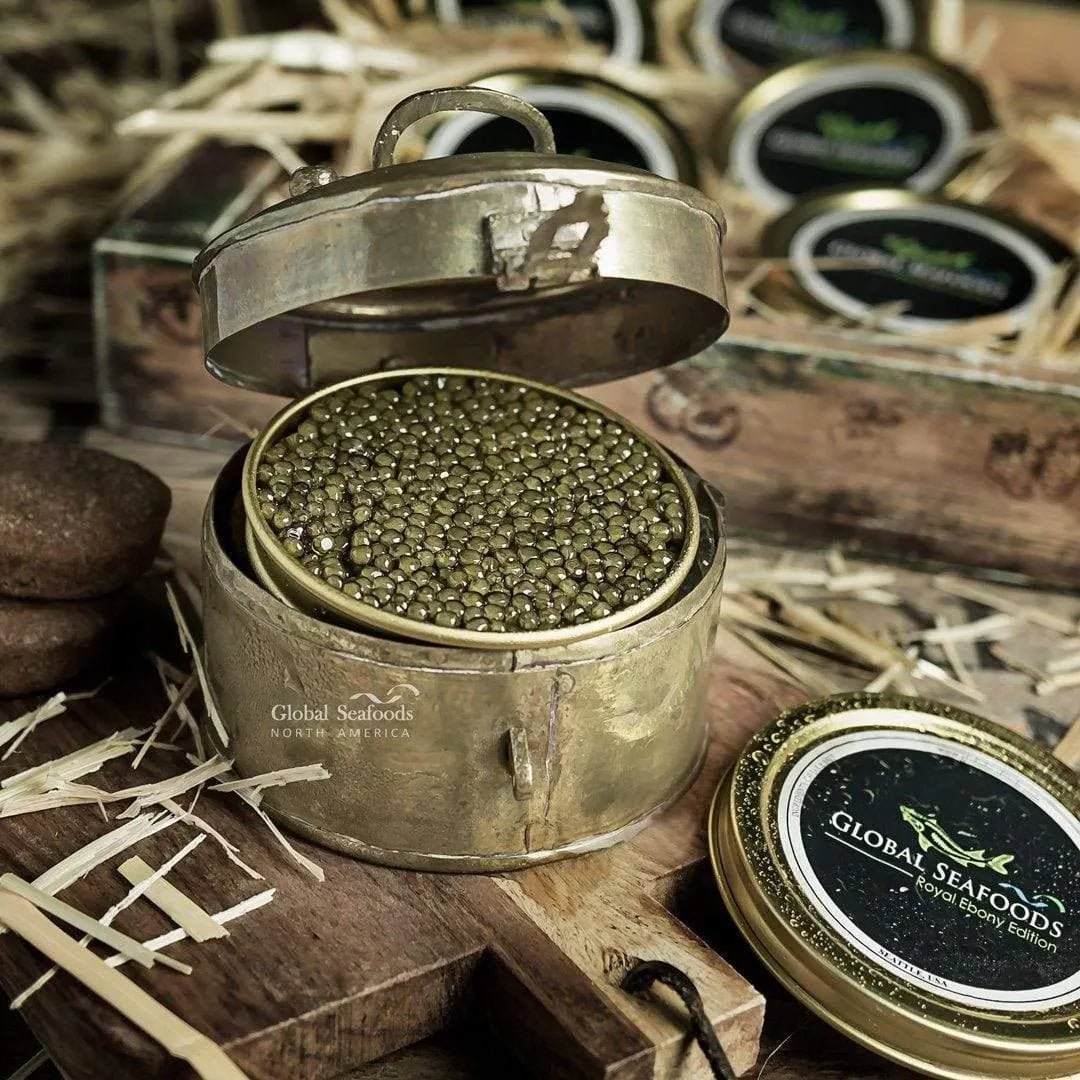 Ossetra caviar in an open tin inside a metal presentation case on a wooden board