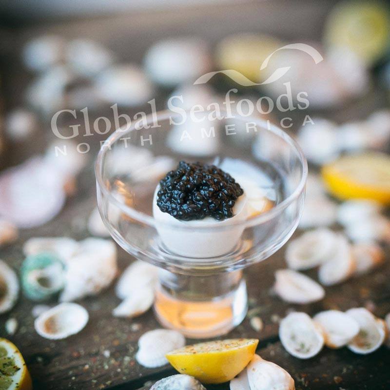 White sturgeon caviar in an eggshell in a glass dish surrounded by seashells and lemon halves