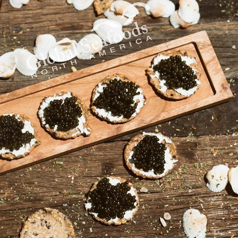 Overhead close-up of Paddlefish caviar on cream-topped crackers beside seashells on a wooden table