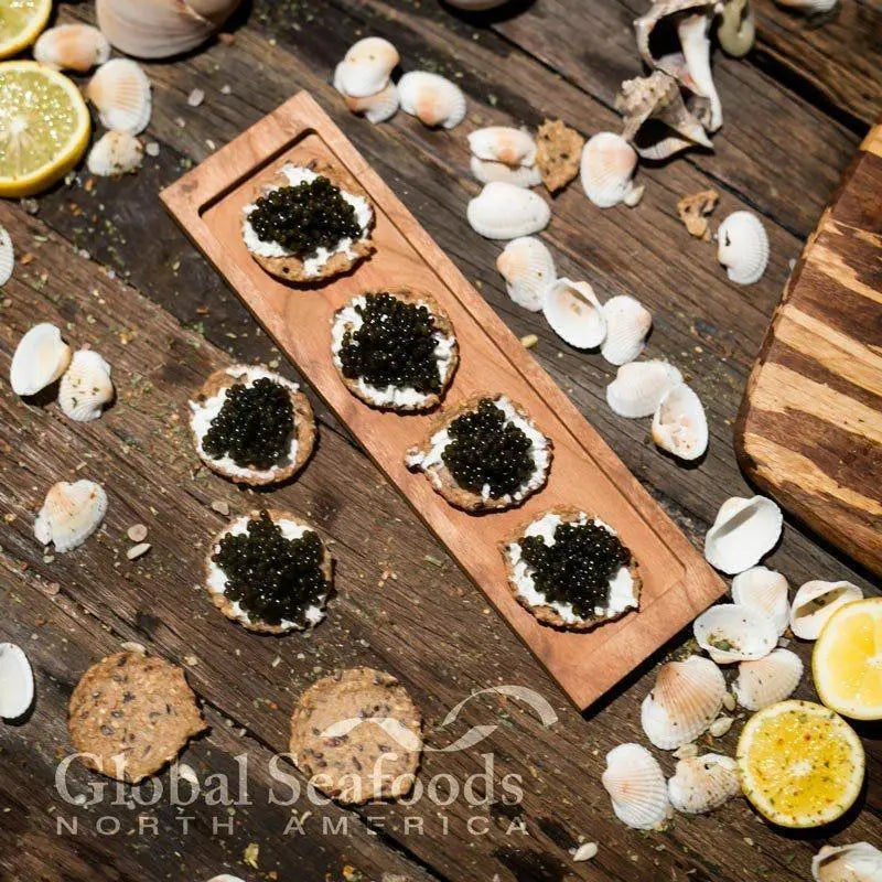 Overhead view of Paddlefish caviar crackers on a wooden board, surrounded by seashells and lemon halves