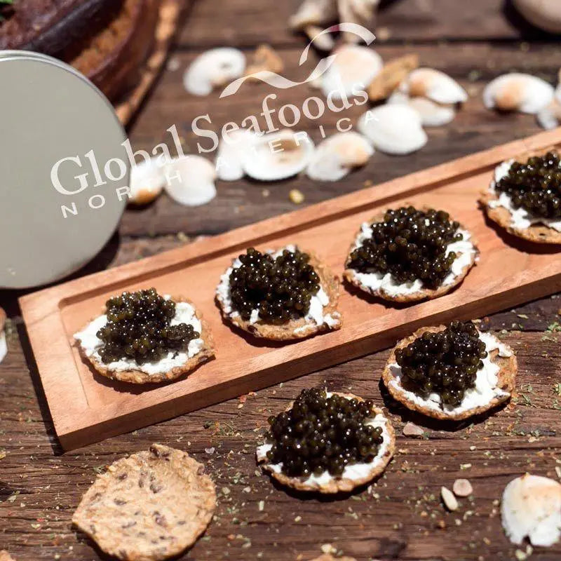 Angled view of Paddlefish caviar on cream-topped crackers, with a wooden serving board and a tin lid